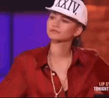 a woman wearing a red shirt and a white hat is sitting in front of a purple background .