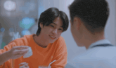 two young men are sitting at a table and talking to each other