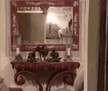 a mirror with a red frame hangs above a table with statues on it