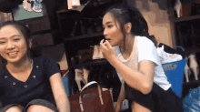 two women are sitting next to each other in front of a shoe rack and one is applying lipstick