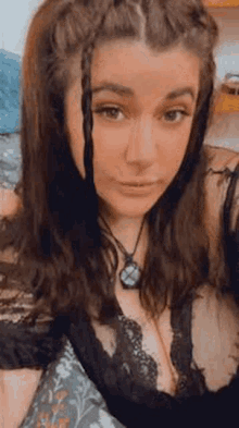 a woman in a black bra and necklace is taking a selfie while laying on a bed .