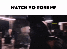 a blurred image of a person walking in a dark room with the words `` watch yo tone mf '' .
