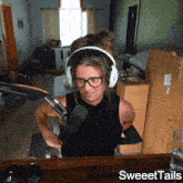 a woman wearing headphones and glasses sits in front of a microphone with sweettails written on the bottom right