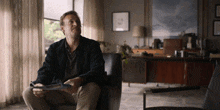 a man sits in a chair with a magazine in his hands