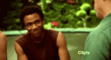 a man in a brown tank top is smiling while talking to another man .