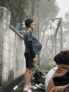 a boy with a huge breast is standing in front of a soccer goal