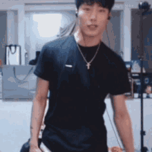 a young man wearing a black t-shirt and a necklace is standing in a room .