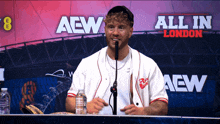 a man speaking into a microphone in front of a banner that says all in london