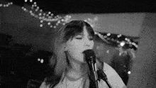 a black and white photo of a girl singing into a microphone .
