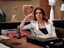 a woman in a white jacket sits at a desk with a bottle of aquafina water