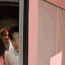 a group of people are standing in a room behind a pink wall .