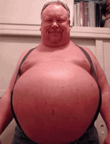 a man with a very large belly is standing in front of a bookshelf .