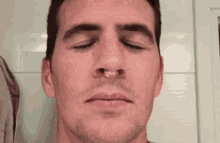 a close up of a man 's face with his eyes closed and a nose ring in his nose .