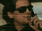 a man wearing sunglasses is talking on a cell phone while driving a car .