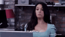 a woman is sitting in front of a laptop computer and says liz wake up