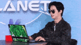 a man wearing sunglasses is typing on a laptop in front of a planet sign