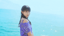 a woman in a purple dress is standing on the beach and smiling at the camera .