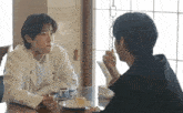 two men are sitting at a table with a plate of food and drinking coffee .