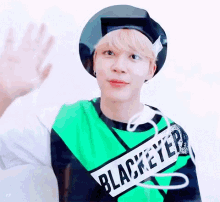 a young man wearing a green shirt and a black hat is waving his hand .