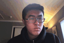 a young man wearing glasses and a black sweater looks at the camera