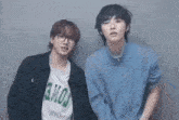 two young men are standing next to each other in front of a wall . one of the men is wearing glasses .