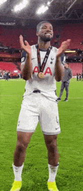 a soccer player is standing on a field with a medal around his neck and clapping his hands .