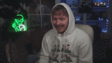a man wearing a white hoodie is sitting in front of a neon sign that says " alien "