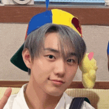 a young man wearing a colorful hat and a white shirt is standing next to a stuffed animal .