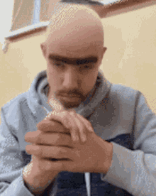 a bald man with a beard is praying with his hands folded in front of him .