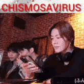 a group of people are sitting at a table looking at their phones with a sign that says chismosaurus in the background