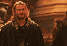 a man with long hair and a beard is standing in front of a crowd of people .