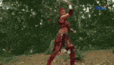 a woman in a warrior costume is standing in the woods with fire coming out of her head .