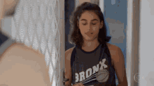 a woman wearing a bronx tank top is standing in front of a door .