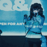 a girl singing into a microphone in front of a screen that says " q & a "