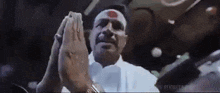 a man with a red spot on his forehead is praying with his hands folded in front of him .
