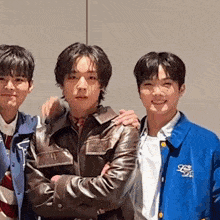 three young men are posing for a picture together . one of the men is wearing a blue jacket .
