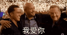 three men are hugging each other in front of a crowd and a sign that says `` i love you '' in chinese .