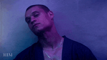 a man wearing a purple shirt and a necklace with the word him below him