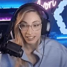 a woman wearing headphones and glasses is standing in front of a microphone .