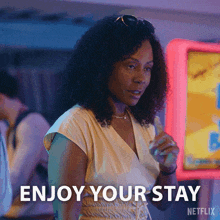 a woman says enjoy your stay while standing in front of a neon sign
