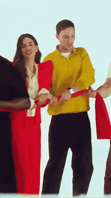 a woman in a red dress is standing next to a man in a yellow sweater