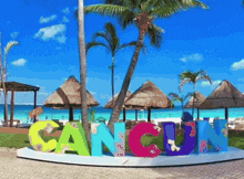 a colorful sign that says cancun in front of a beach with palm trees