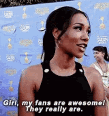 a woman is standing in front of a blue wall and saying `` girl , my fans are awesome ! they really are . ``