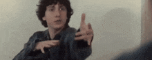 a young man in a denim jacket is making a gesture with his hand .