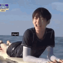 a man is laying on a surfboard in the ocean with a sign that says aigo
