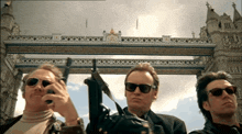 three men are standing in front of a bridge with a clock on it