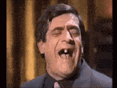 a man with a missing tooth is wearing a suit and tie and making a funny face .
