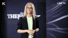 a woman with blonde hair and glasses stands in front of a line tv logo
