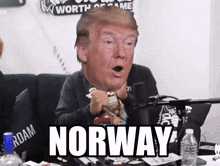 a man sitting in front of a microphone with a donald trump head on his head and the word norway written on the table