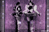 two women in costume are dancing in front of a purple curtain